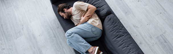 Top view of man suffering from bellyache on couch, banner  - Photo, Image