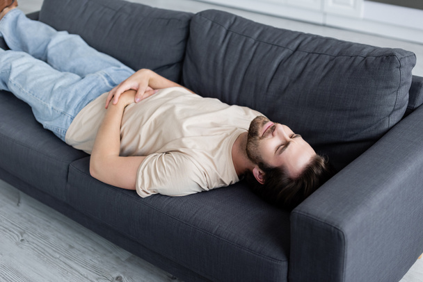 Tired man suffering from stomachache on couch - Фото, изображение