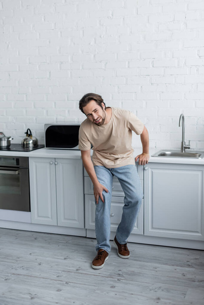 Diseased man touching knee on kitchen - Photo, Image