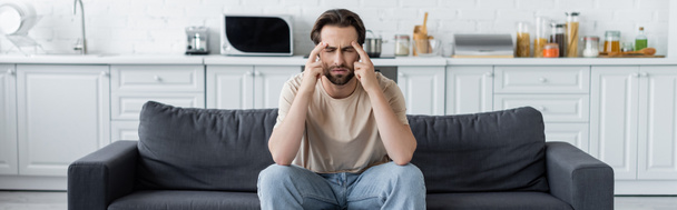 Man suffering from headache on couch in kitchen, banner  - Foto, Imagem