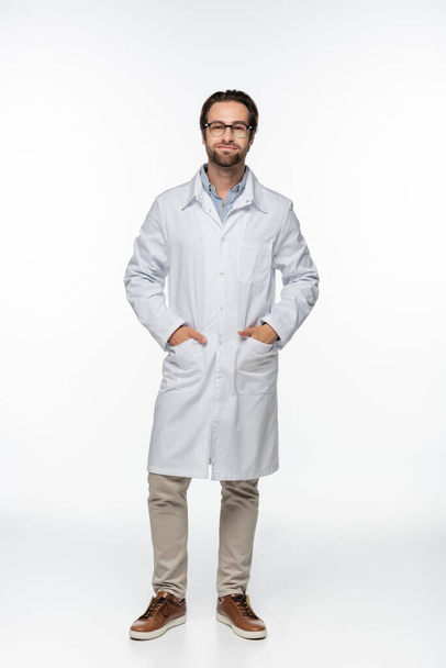 Doctor in eyeglasses and coat looking at camera on white background  - Valokuva, kuva
