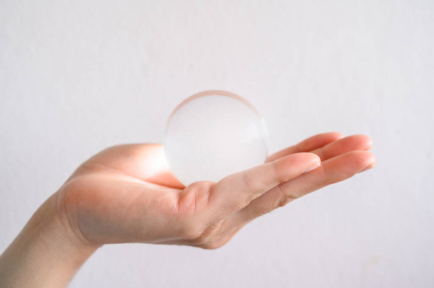 Gros plan de quelqu'un tenant une boule de cristal transparente claire. L'utilisation de boules de cristal pour prédire l'avenir est considérée comme une pseudoscience. - Photo, image