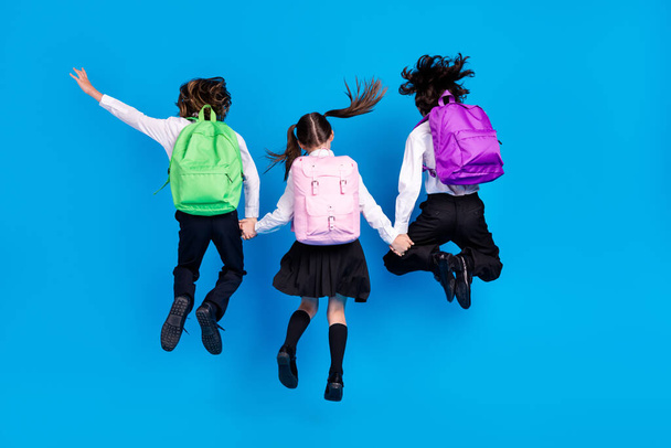 Photo of funky funny schoolkids formalwear backpacks smiling jumping high holding arms isolated blue color background - Foto, afbeelding