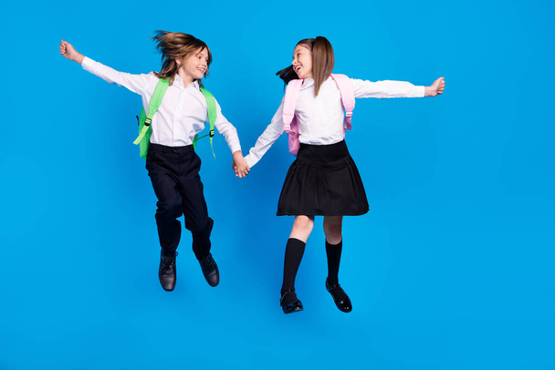 Photo of excited funky schoolkids formalwear backpacks smiling jumping high looking eyes isolated blue color background - Foto, afbeelding