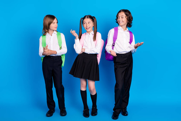 Photo of positive classmates children have conversation wear backpack uniform isolated blue color background - Valokuva, kuva