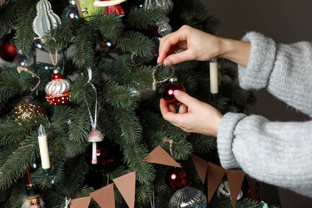 Рука жінки прикрашає ялинку новорічними та різдвяними іграшками. Жіноча рука прикрашає ялинку кульками. Новорічний настрій. Різдвяна підготовка
. - Фото, зображення