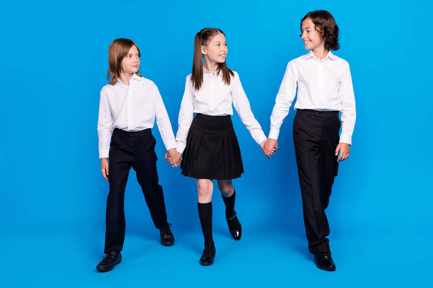 Photo of pretty charming schoolkids formalwear smiling holding arms walking looking isolated blue color background - Fotó, kép