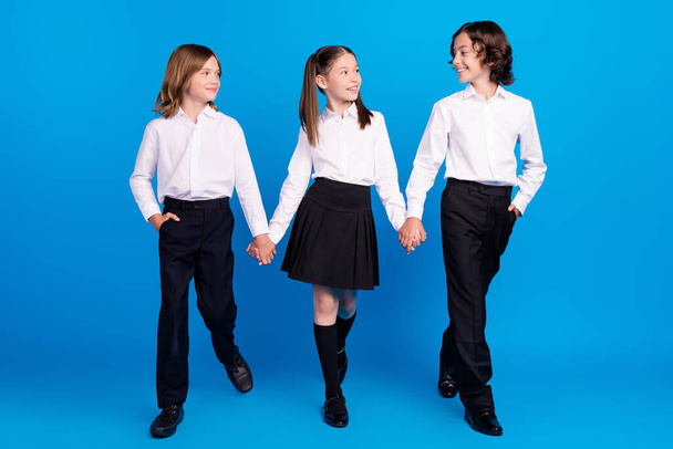 Photo of friendly classmates schoolkids hold hands walk enjoy wear uniform isolated blue color background - Fotografie, Obrázek