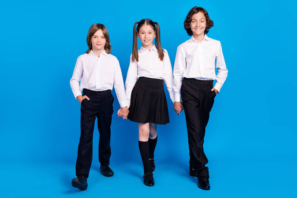 Photo of sweet shiny schoolchildren wear uniform holding arms walking smiling isolated blue color background - Fotó, kép
