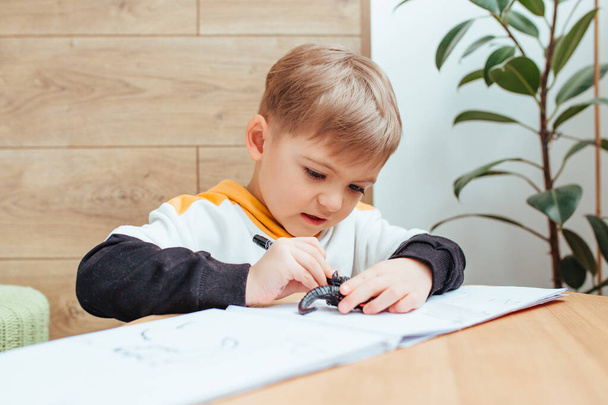 un chico rubio está jugando con un kit de construcción, con una pared de madera en el fondo. - Foto, Imagen