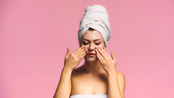 young woman with white towel on head applying exfoliating mask isolated on pink - Photo, Image