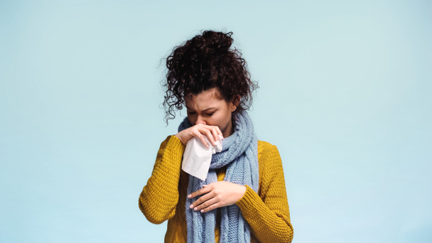 больная женщина в теплом свитере вытирает нос бумажной салфеткой, изолированной на голубом - Фото, изображение
