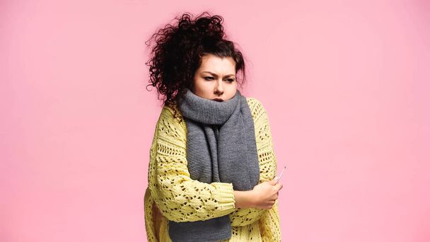 ill woman in warm sweater and scarf holding thermometer isolated on pink - Foto, Imagem