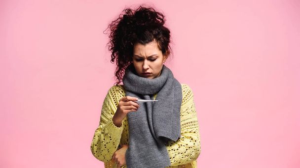 displeased woman in scarf and sweater looking at thermometer isolated on pink - Photo, Image