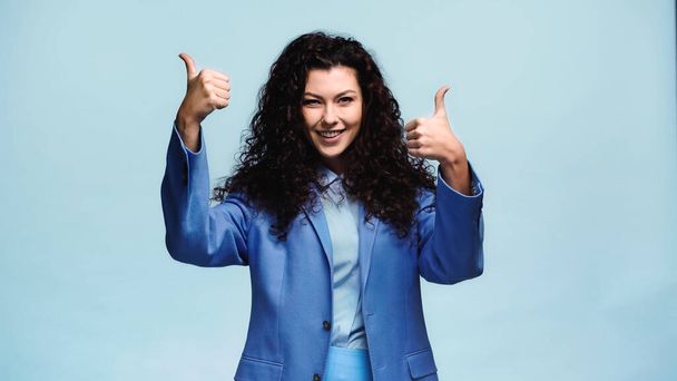 cheerful woman showing thumbs up while looking at camera isolated on blue - Zdjęcie, obraz