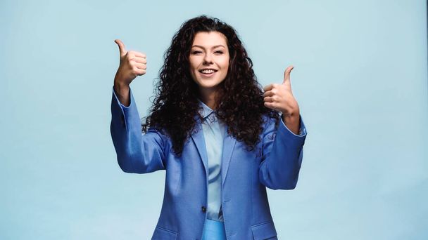 joyful brunette woman showing thumbs up isolated on blue - Foto, afbeelding