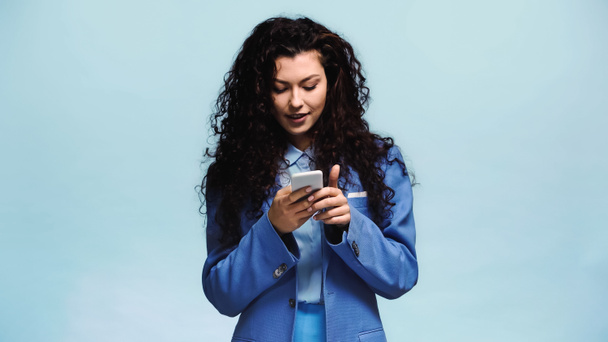 young and happy woman messaging on mobile phone isolated on blue - Photo, Image