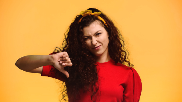 недовольная женщина с вьющимися волосами показывает палец вниз изолированы на оранжевый - Фото, изображение