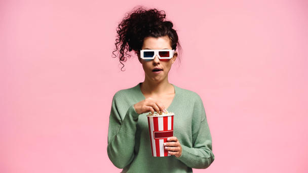 impressed woman in 3d glasses eating popcorn isolated on pink - Photo, Image