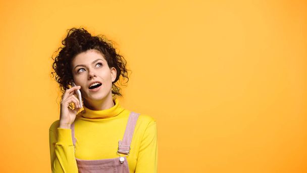surprised woman looking away during conversation on cellphone isolated on orange - Foto, immagini