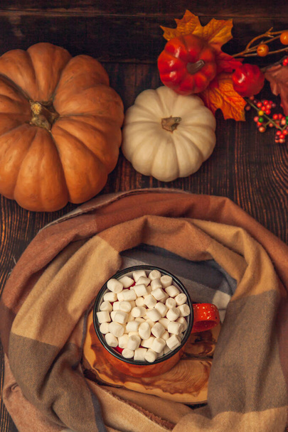 Autumn decor on a wooden background: a mug with cocoa and marshmallows, a checkered scarf, pumpkins and autumn leaves, top view flat lay - Foto, Bild