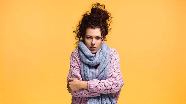 dissatisfied woman freezing in knitted sweater and scarf isolated on orange - Фото, изображение