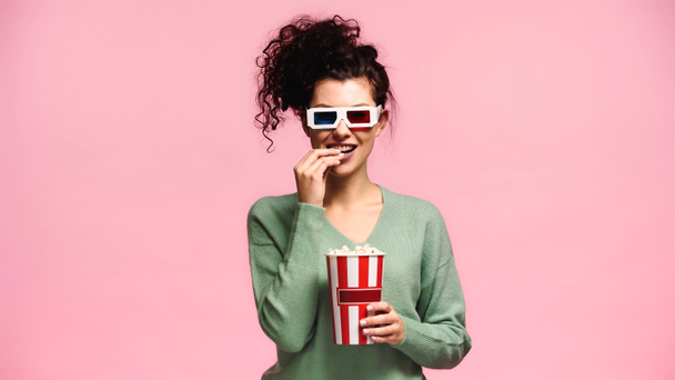 緑のトレーナーとピンクに隔離されたポップコーンを食べる3Dメガネの陽気な女性 - 写真・画像