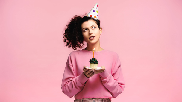 mulher sonhadora fazendo desejo enquanto segurando cupcake aniversário isolado em rosa - Foto, Imagem