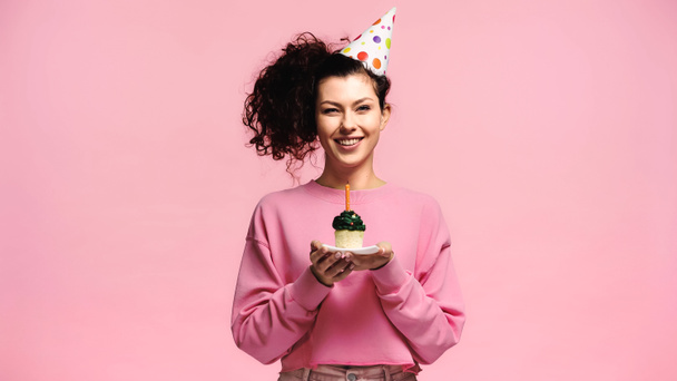 mujer emocionada con cupcake cumpleaños sonriendo a la cámara aislado en rosa - Foto, imagen