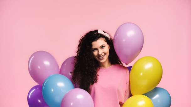 χαρούμενη γυναίκα με πολύχρωμα μπαλόνια κοιτάζοντας κάμερα απομονωμένη σε ροζ - Φωτογραφία, εικόνα