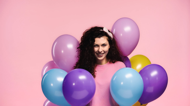 joyeuse femme souriant à la caméra près de ballons multicolores isolés sur rose - Photo, image