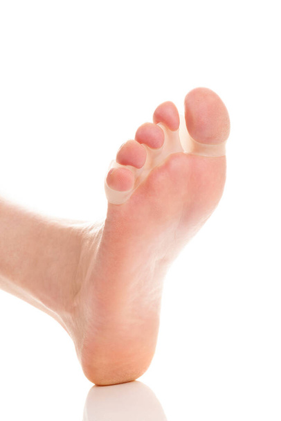 Nackte Füße in Ballenkorrektoren zur Behandlung von Schmerzen bei Hallux valgus auf weißem Hintergrund. - Foto, Bild
