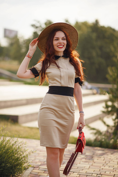 A happy young woman, holding a wide hat, poses in a park in summer - Foto, imagen