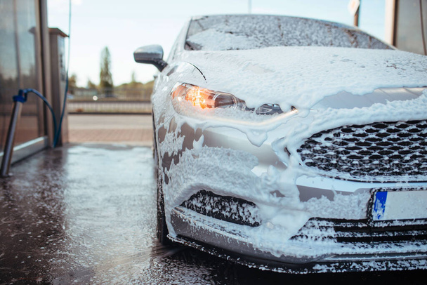 a gray sedan stands in soapy foam at a self-service car wash - Fotó, kép