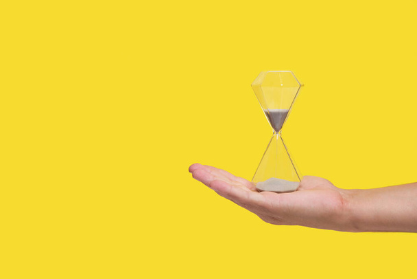 An hourglass on palm of your hand, yellow background, concept of loss and old age passing time - Fotoğraf, Görsel