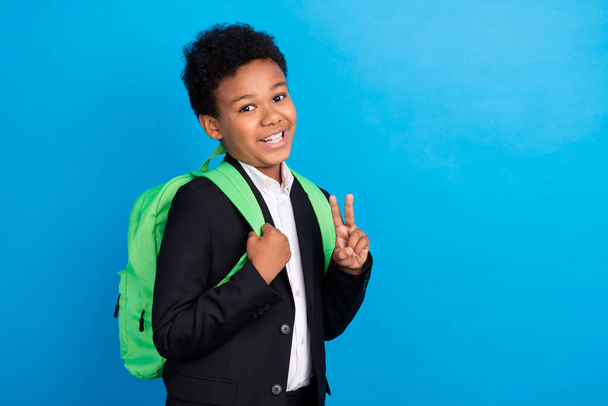 Photo of young happy cheerful dark skin boy smile good mood v-sign wear bag isolated on blue color background - Φωτογραφία, εικόνα