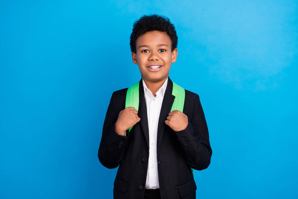 Photo of young happy positive dark skin boy good mood wear backpack smile pupil isolated on blue color background - Foto, immagini
