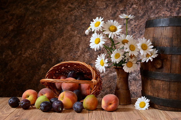 Fleurs de marguerite dans un vase avec des fruits frais dans un panier vicker
 - Photo, image