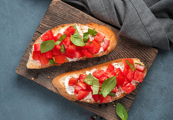 Two sandwiches with fried toast, tomatoes, cheese and basil on a gray-blue background. Italian bruschetta. Top view, close-up. - Photo, Image