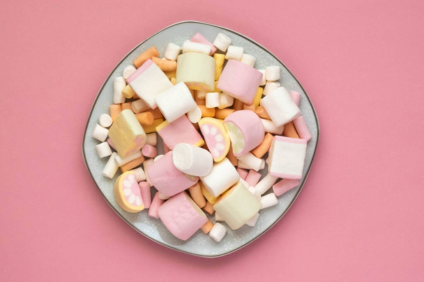 Πολύχρωμα ζαχαρωτά σε μια λευκή τετράγωνη πλάκα, απομονωμένα σε ροζ φόντο. Κοντινό πλάνο της υφής αφράτου ζαχαρωτού. - Φωτογραφία, εικόνα