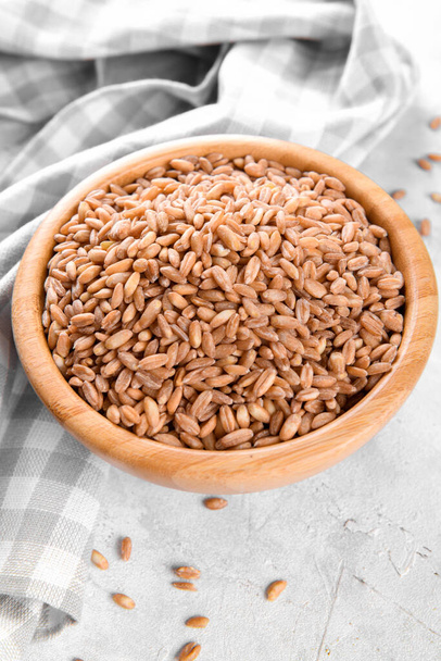 Farro d'épeautre cru à grains entiers dans un bol en bois sur fond de table en pierre grise, fond de céréales alimentaires, gros plan - Photo, image