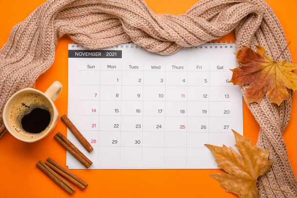 Calendario con taza de café, bufanda y hojas de otoño sobre fondo de color - Foto, imagen