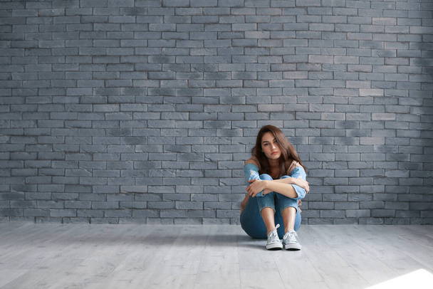 Депрессивная молодая женщина сидит у кирпичной стены
 - Фото, изображение