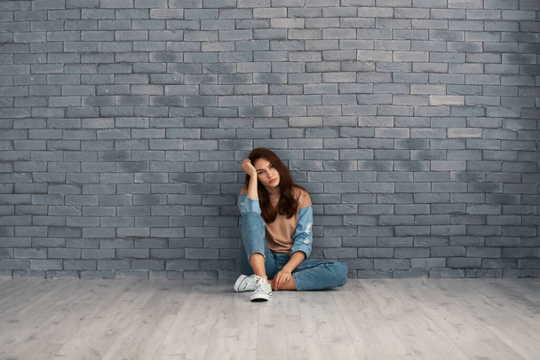 Депрессивная молодая женщина сидит у кирпичной стены
 - Фото, изображение