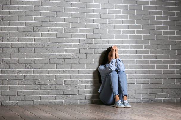 Depressed young woman sitting near brick wall - Фото, изображение