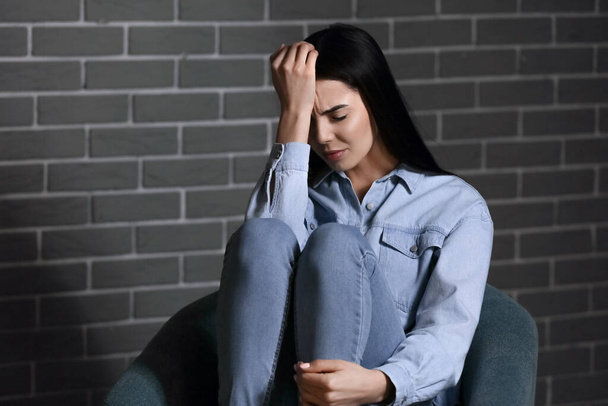 Depressieve jonge vrouw zit in de buurt van baksteen muur - Foto, afbeelding