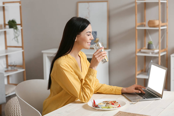 Belle jeune femme avec ordinateur portable manger quesadilla savoureux à la maison - Photo, image