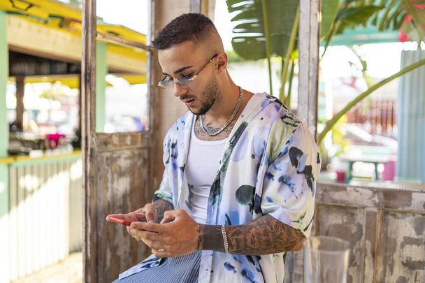 A side view of a Spanish bearded attractive young male in stylish clothes typing on his phone - 写真・画像