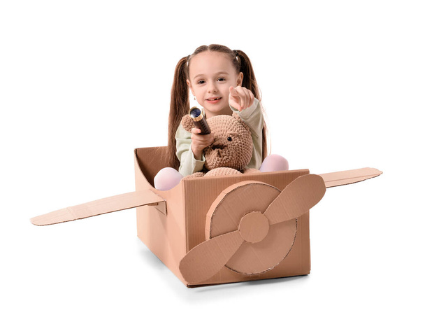 Klein meisje spelen met speelgoed en karton vliegtuig op witte achtergrond - Foto, afbeelding