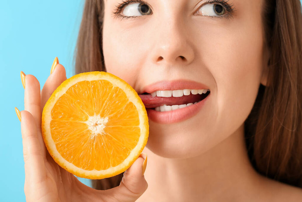 mooie jonge vrouw met sappige oranje op kleur achtergrond, close-up - Foto, afbeelding